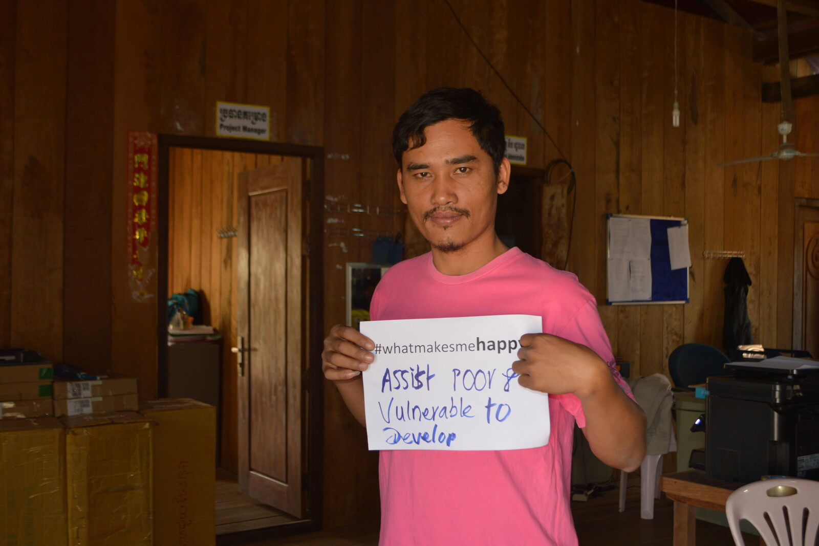Ein Mann hält einen Zettel hoch mit der Aufschrift "#whatmakesmehappy - Assist poor vulnerable to develop"