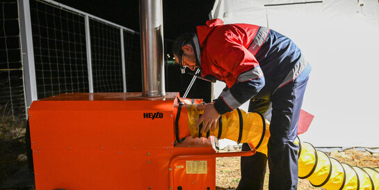 Ein Malteser-Helfer schließt einen Schlauch an einem Heizlüfter an