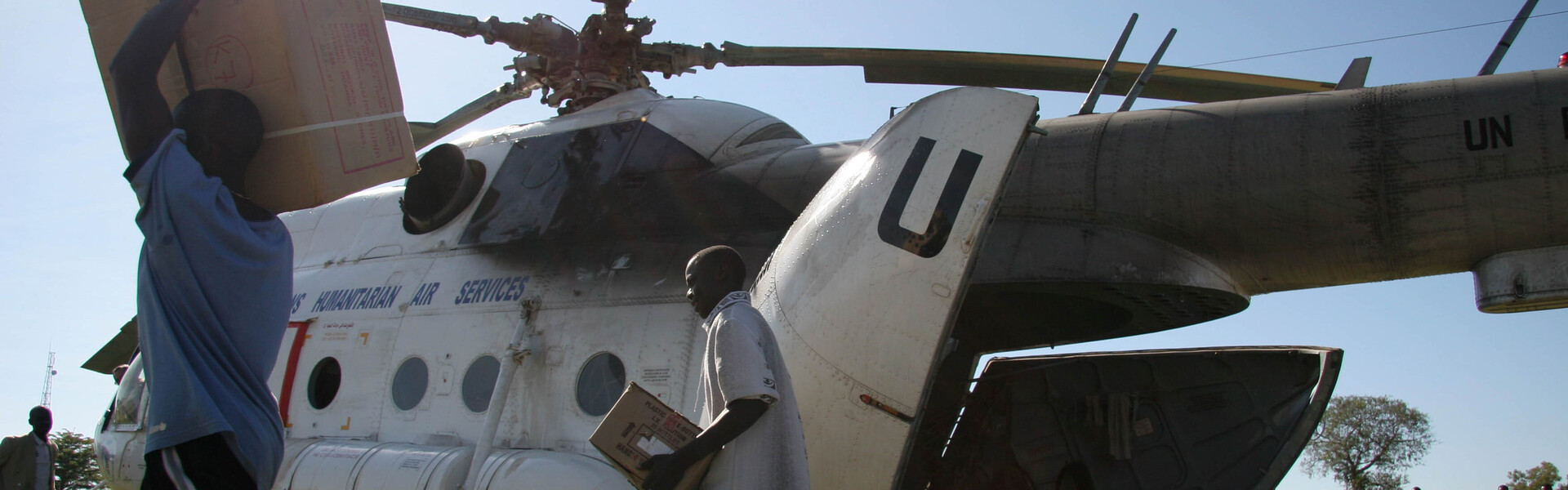 In Uganda werden nach der großen Flut Hilfsgüter aus einem Hubschrauber durch Männer ausgeladen.
