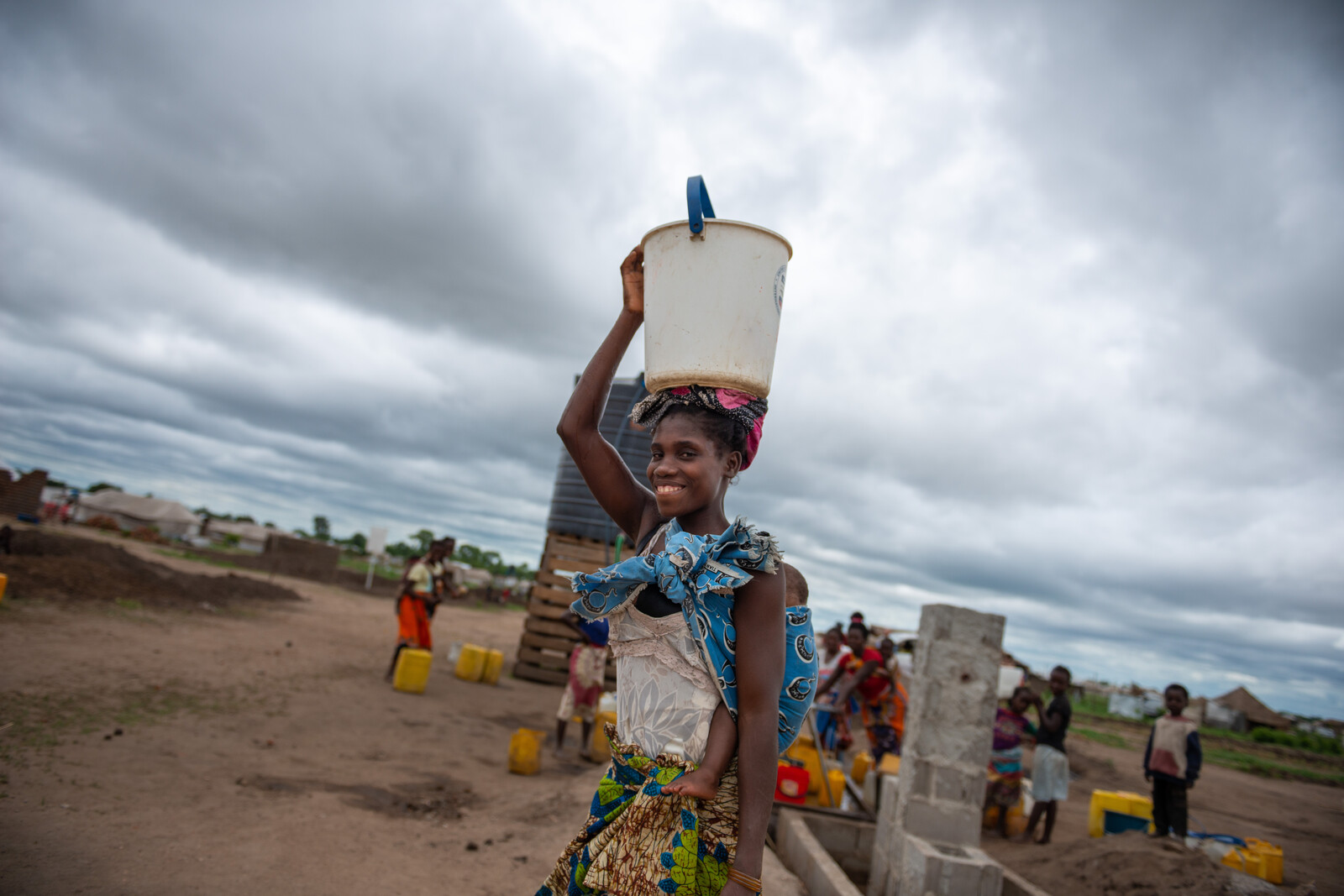 Eine Frau in Mosambik mit Wassereimer auf dem Kopf und Baby auf dem Rücken