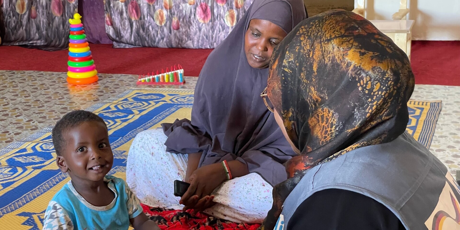 Ein Junge und zwei Frauen sitzen im Senegal auf einem Teppichboden
