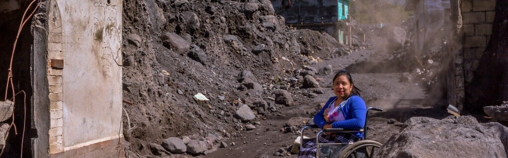 Eine Frau in Guatemala sitzt im Rollstuhl, umgeben von Trümmern