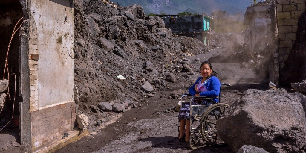 Eine Frau in Guatemala sitzt im Rollstuhl, umgeben von Trümmern