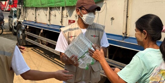 Ein Helfer verteilt in Myanmar Wasser an eine Frau