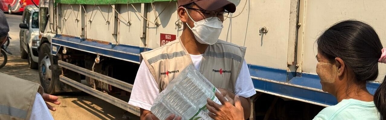 Ein Helfer verteilt in Myanmar Wasser an eine Frau