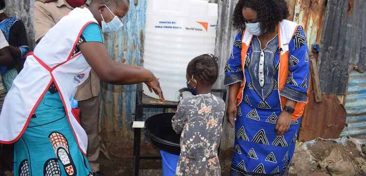 Helferinnen in Kenia mit einem Kind beim Händewaschen