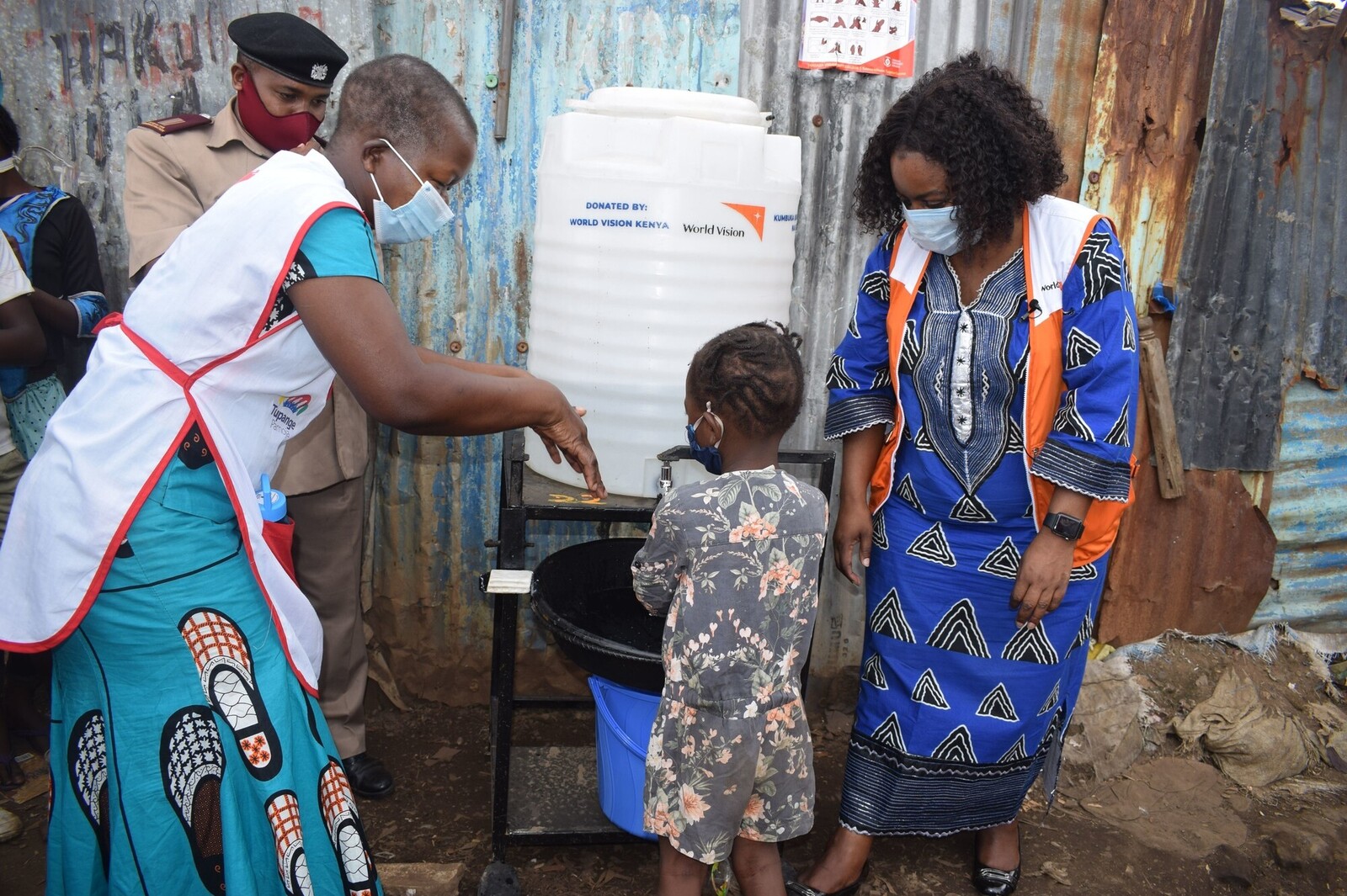 Helferinnen in Kenia mit einem Kind beim Händewaschen