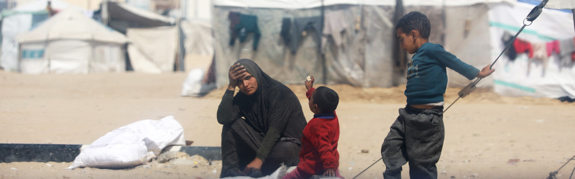 Eine Frau sitzt mit ihren Kindern auf dem Boden eines Zeltlagers