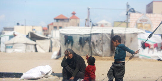 Eine Frau sitzt mit ihren Kindern auf dem Boden eines Zeltlagers