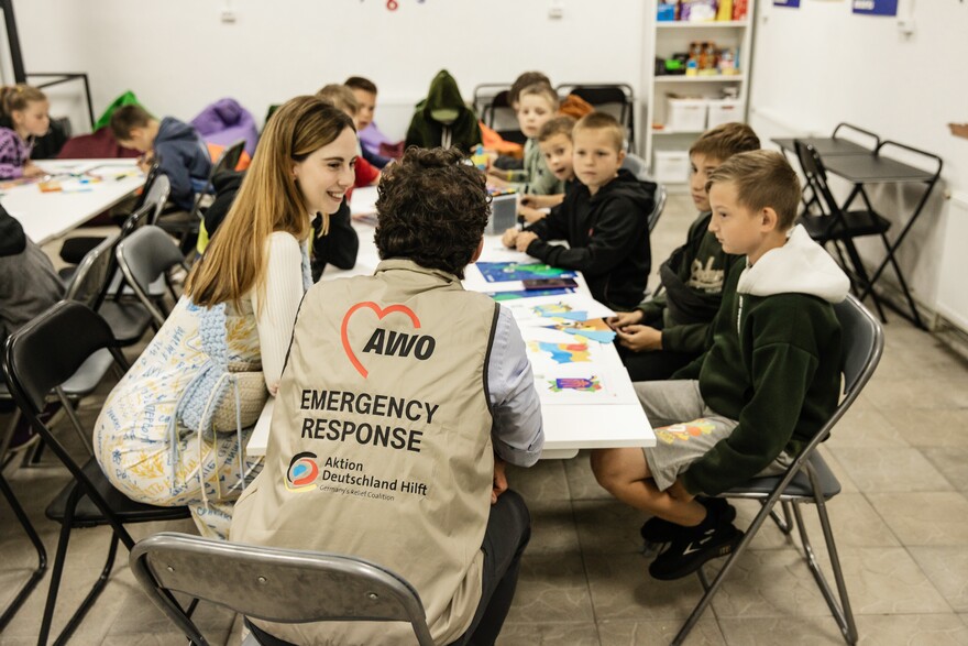 Ein Helfer von AWO International sitzt in der Ukraine mit Kindern an einem Tisch