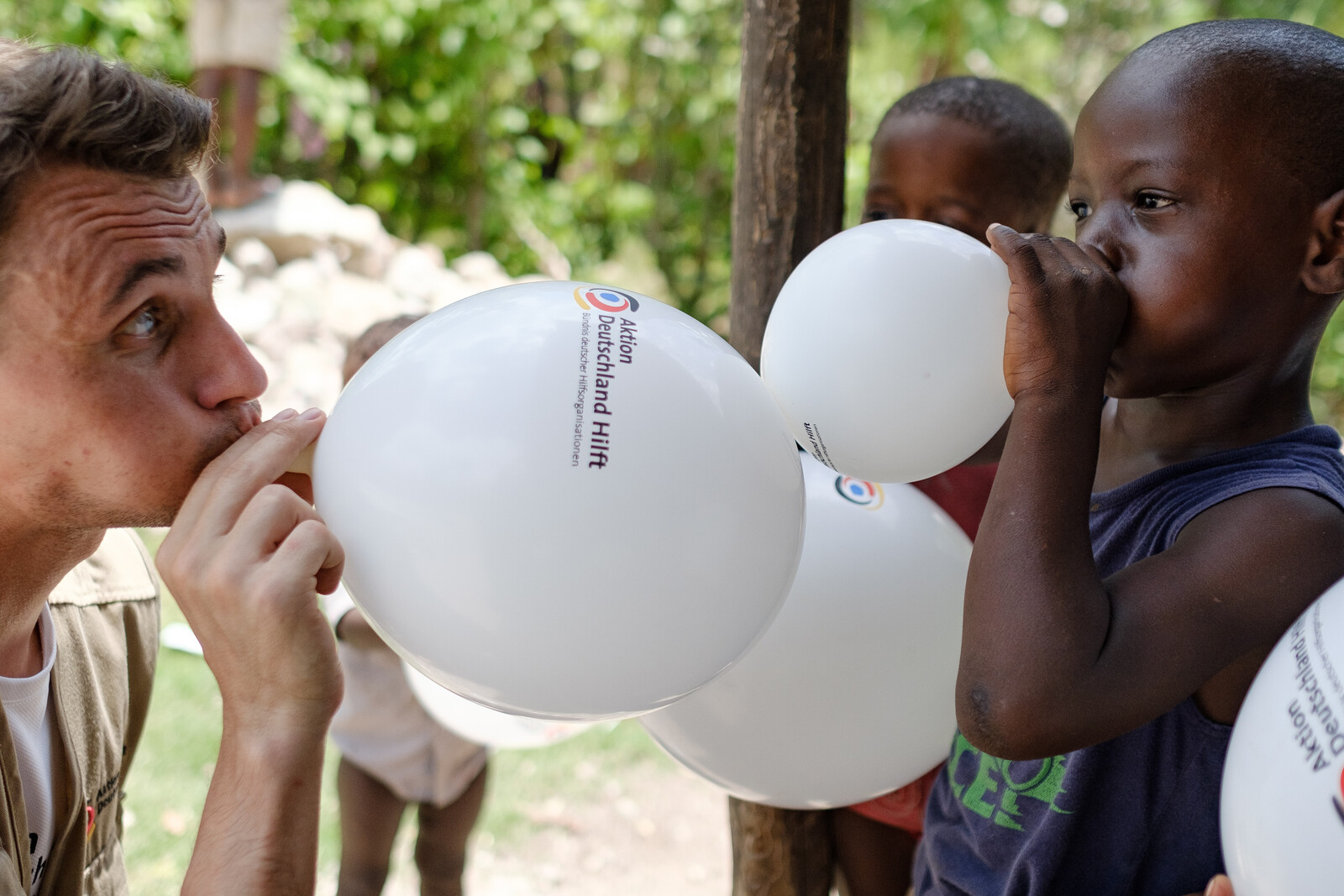 Ein Helfer bläst mit Kindern Luftballons auf