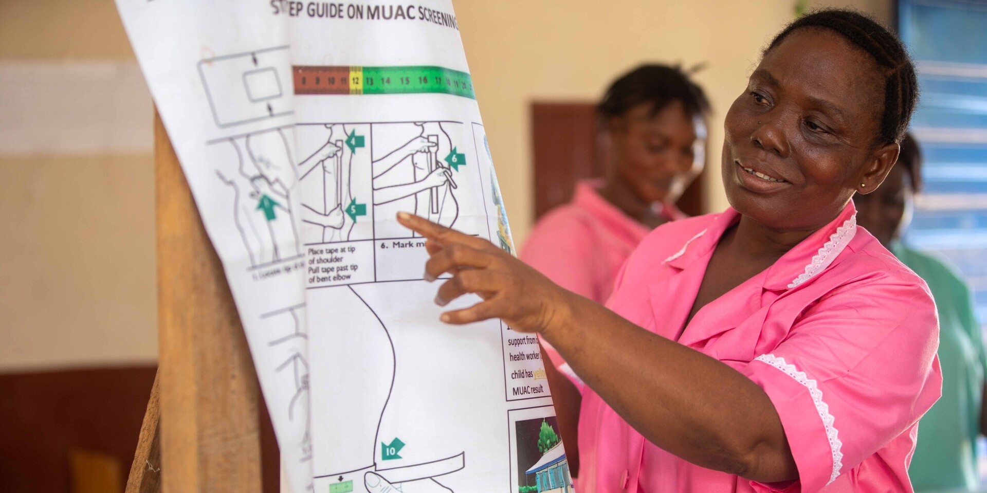 Eine Frau erklärt in Sierra Leone mithilfe eines Informationsplakats, wie ein MUAC-Band zur Erkennung von Unterernährung eingesetzt wird Eine Frau erklärt in Sierra Leone mithilfe eines Informationsplakats, wie ein MUAC-Band zur Erkennung von Unterernährung eingesetzt wird