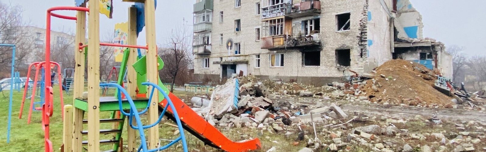 Ein von Bomben zerstörter Spielplatz und Wohnhaus in der Ukraine
