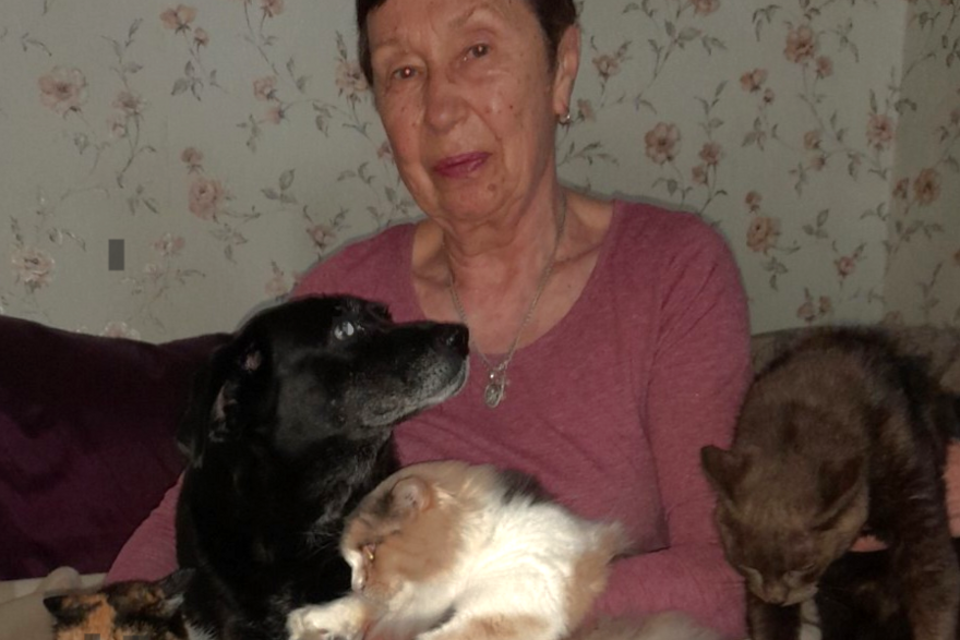 Eine ältere Frau mit drei Katzen und einem Hund in ihren Armen