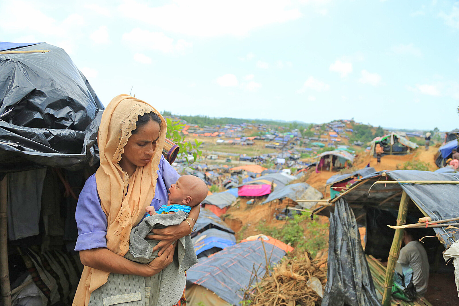 Eine Frau hält ihr Baby vor einer Notunterkunft im Rohingya-Lager im Arm 