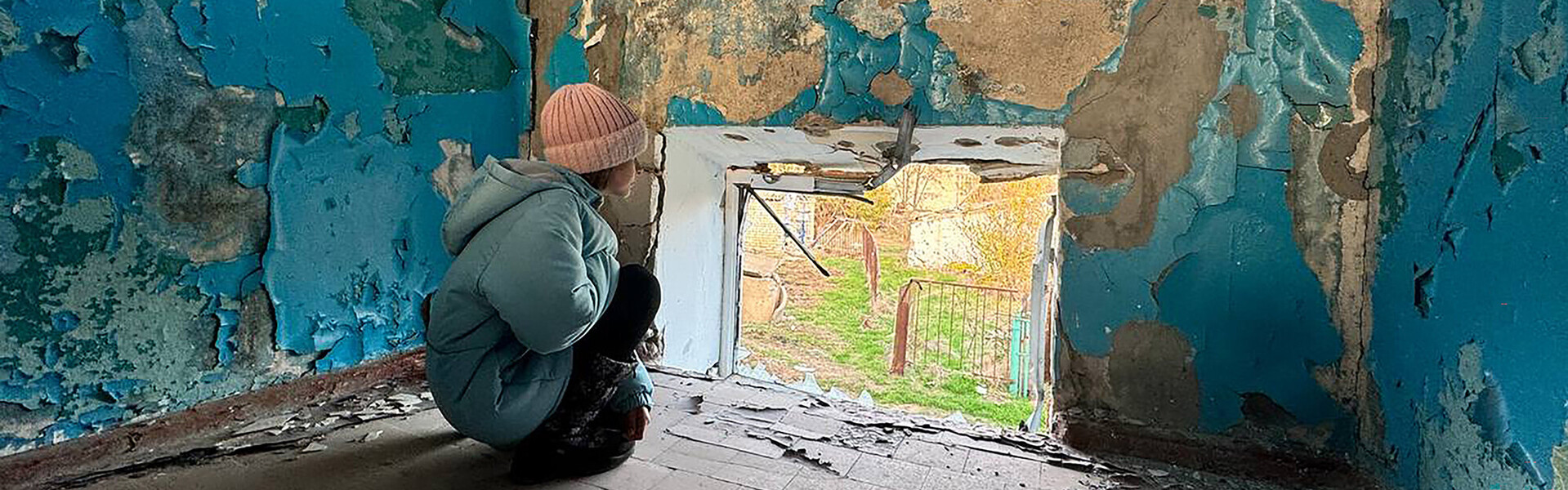 Ein Kind schaut aus dem Fenster einer zerstörten Schule in der Ukraine