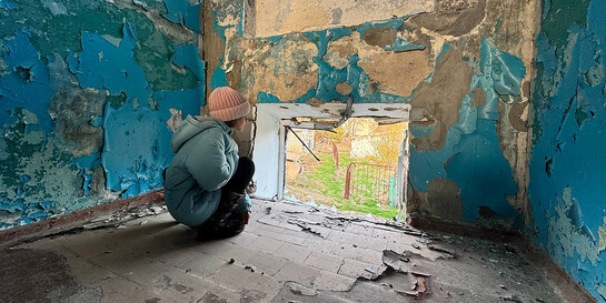 Ein Kind schaut aus dem herausgesprengten Fenster eines im Krieg stark beschädigten Gebäudes