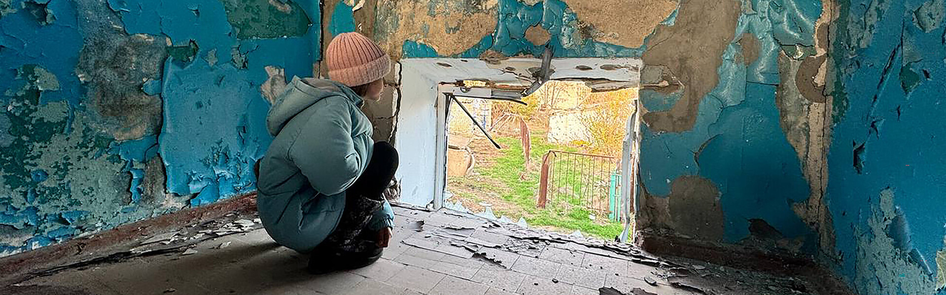 Ein Kind schaut aus dem Fenster einer zerstörten Schule in der Ukraine