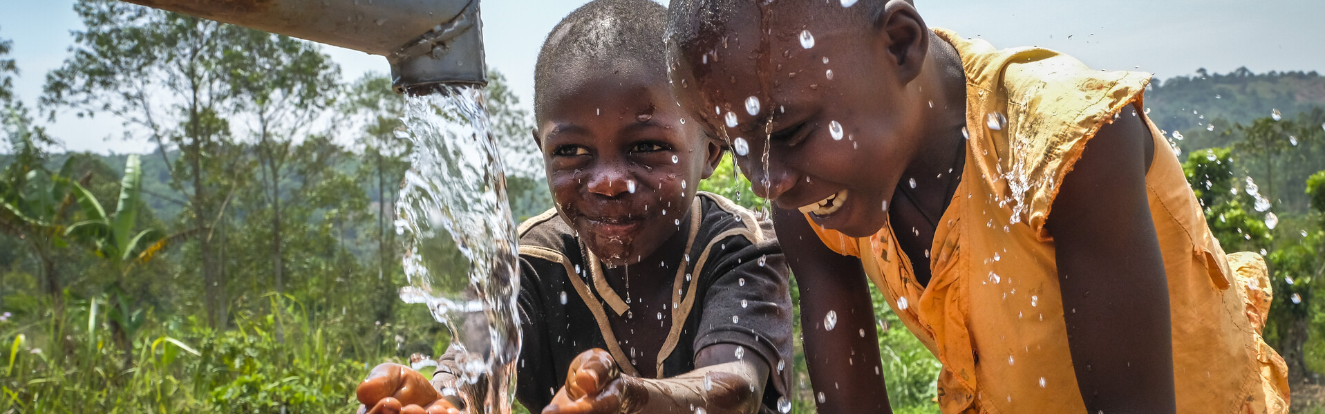 Zwei Kinder in Uganda freuen sich über frisches Trinkwasser 
