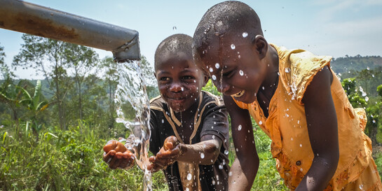 Zwei Kinder in Uganda freuen sich über frisches Trinkwasser 
