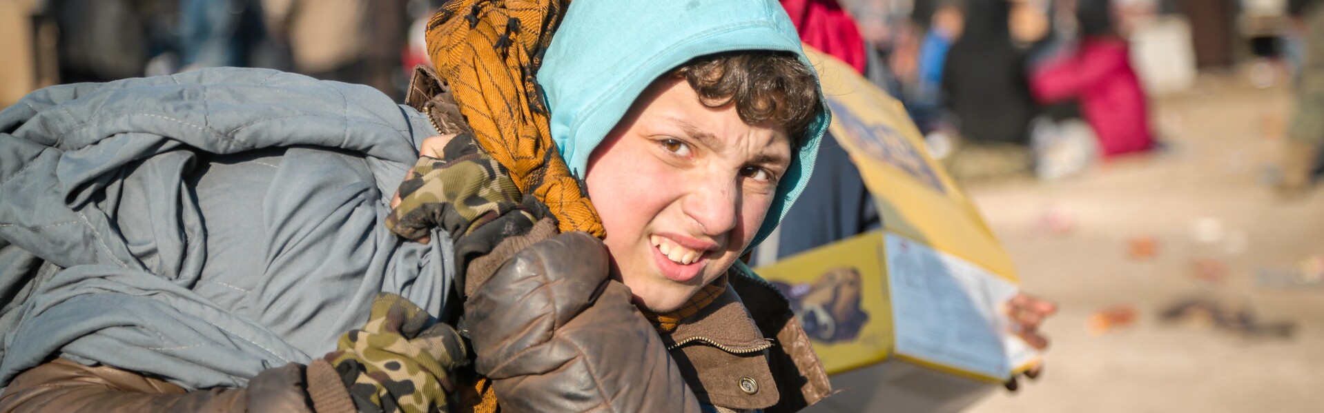 In Syrien steht ein Kind mit Gepäck. Es ist ein von der Flüchtlingskrise betroffen