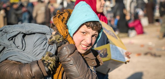 In Syrien steht ein Kind mit Gepäck. Es ist ein von der Flüchtlingskrise betroffen