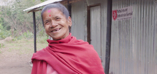 Eine Frau steht vor einem Haus in Nepal nach dem Erdbeben in 2015.