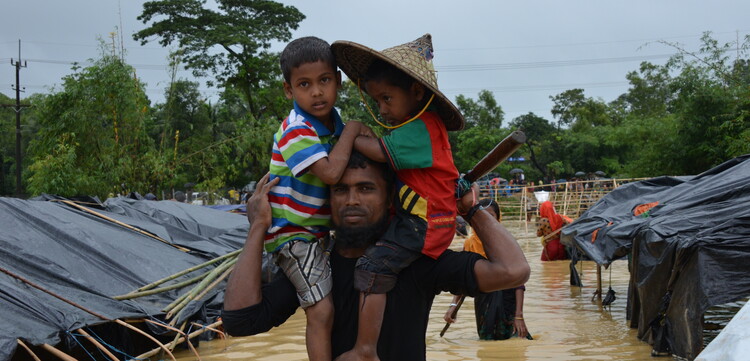 Ein Mann mit seinen Kindern in einem überfluteten Flüchtlingscamp in Bangladesch