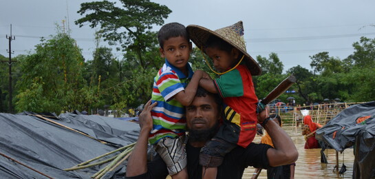 Ein Mann mit seinen Kindern in einem überfluteten Flüchtlingscamp in Bangladesch