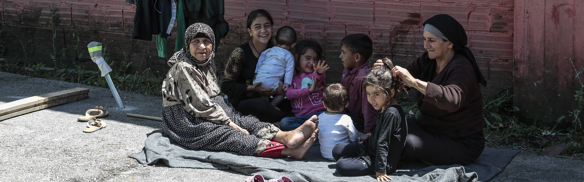 Vor einer Mauer sitzen Frauen und Mädchen. Sie sind Betroffene des Krieges in Syrien.