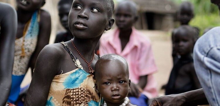 Ein Mann misst den Grad der Unterernährung bei einem Kind. Es sitzt bei seiner Mutter auf dem Schoß