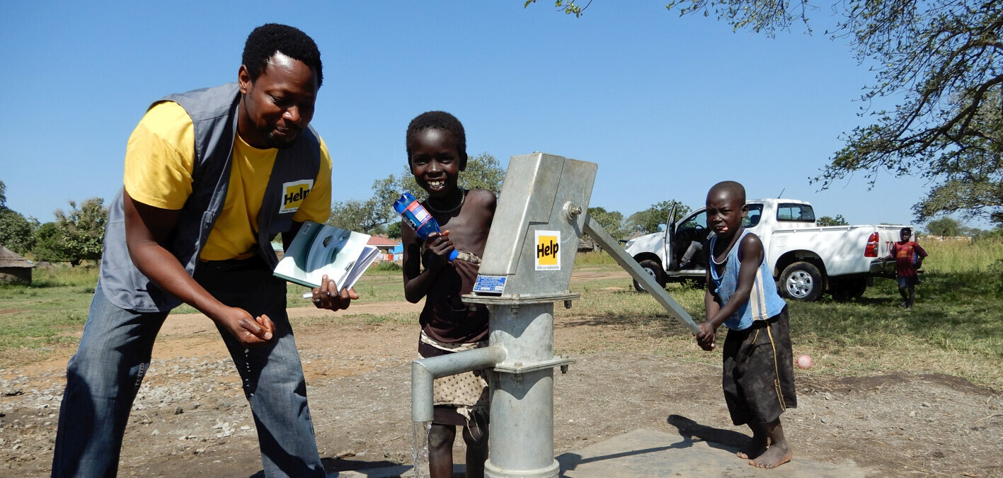 Helfer Ferndandez Sajero Lucheveleli mit Kindern im Südsudan an einem neu gebauten Brunnen Helfer Ferndandez Sajero Lucheveleli mit Kindern im Südsudan an einem neu gebauten Brunnen