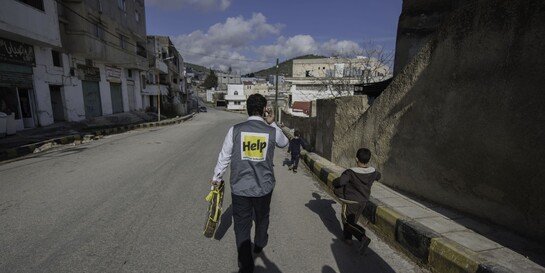 Ein Helfer und zwei Kinder laufen eine Straße in Syrien entlang (Symbolbild)