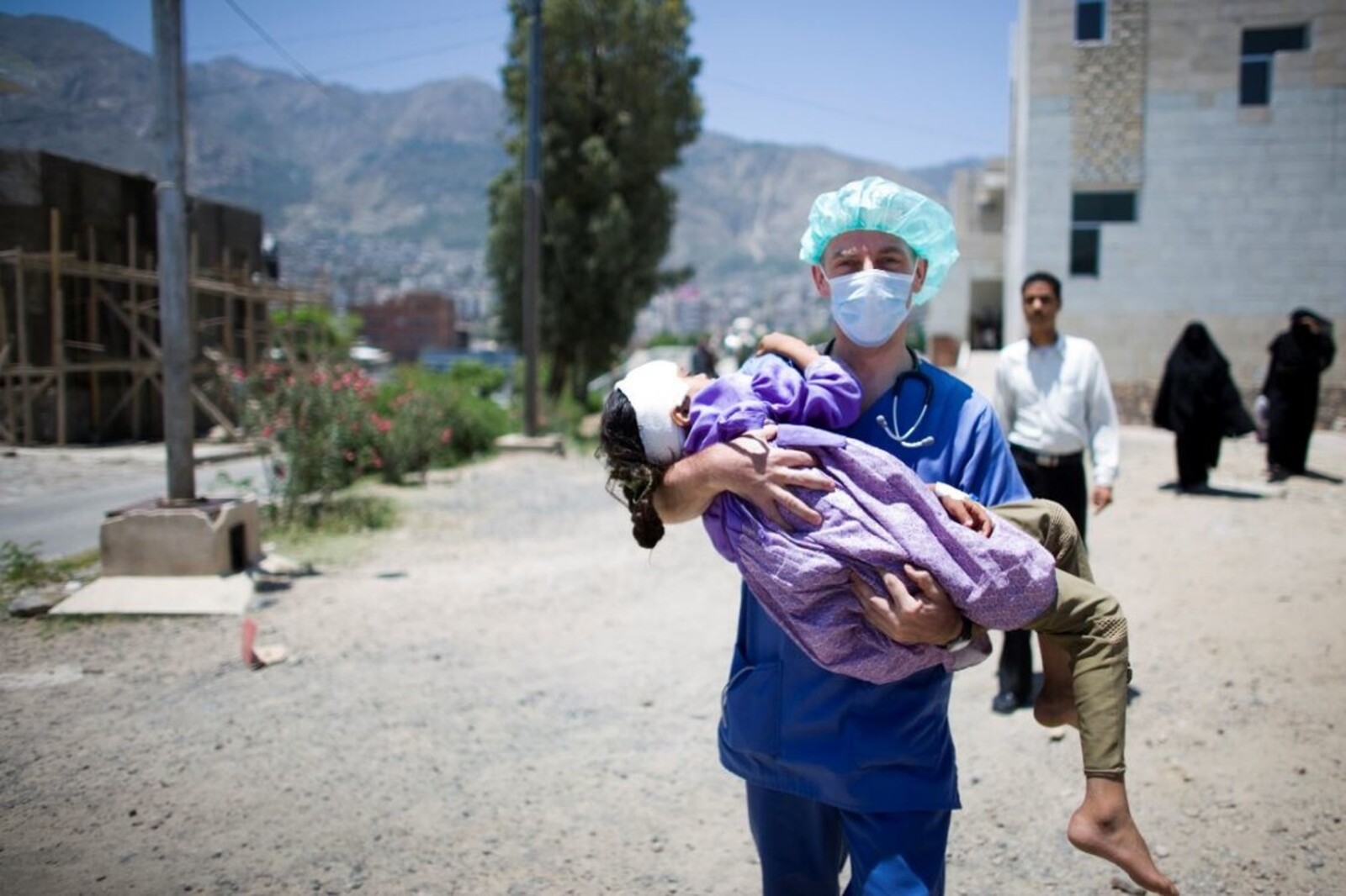 Arzt im Jemen hält kleines Mädchen mit Kopfverband im Arm