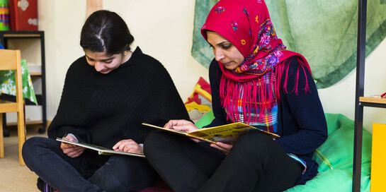 Zwei geflüchtete Frauen lesen in einer Unterkunft