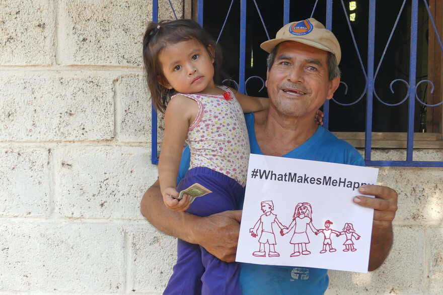 In Guatemala hält ein Mann, mit Kind im Arm, ein Zettel mit der Aufschrift "#whatmakesmehappy" und dass ihm die Familie am wichtigsten ist