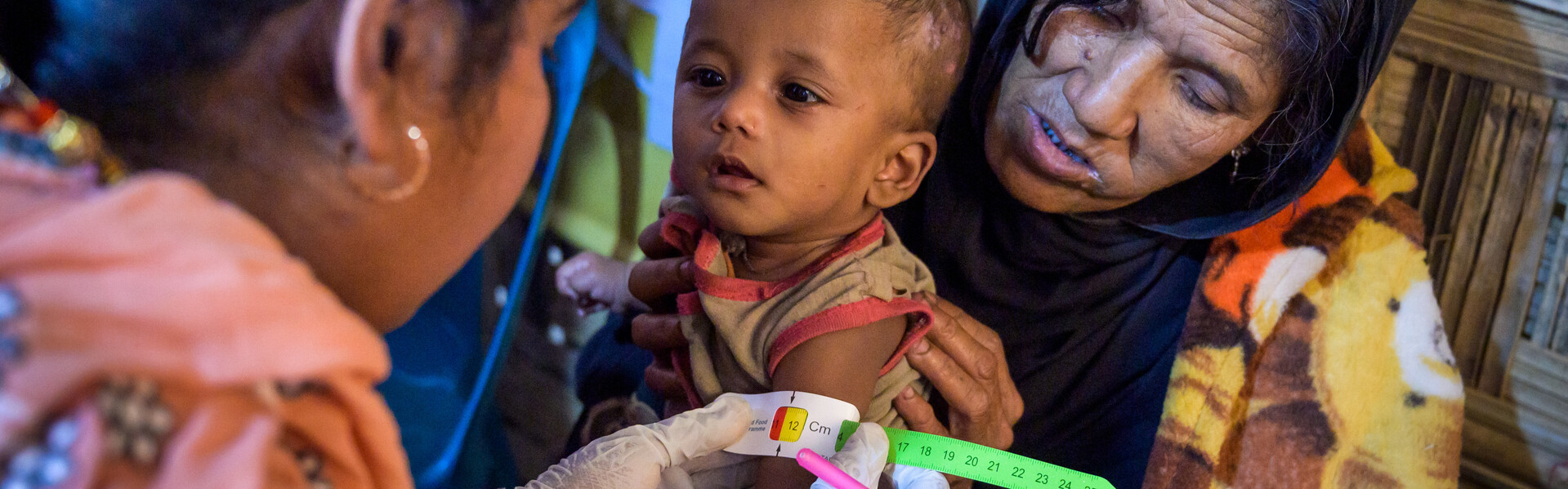 Ein kleines Rohingya-Mädchen wird von ihrer Oma festgehalten, während eine Ärztin ihren Grad der Unterernährung mit dem Hungermaßband feststellt
