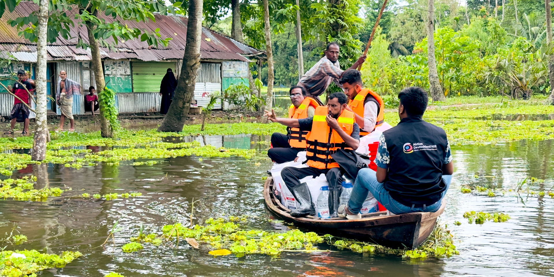 Helfer:innen transportieren Trinkwasser und Lebensmittel in einem überfluteten Gebiet in Bangladesch