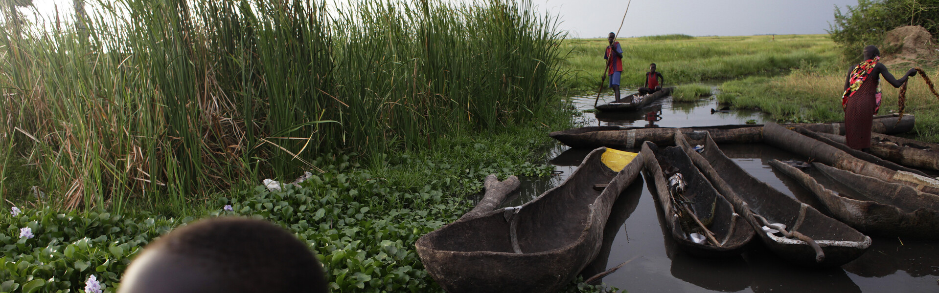 Kind steht im Vordergrund, Boote sind im Hintergrund zu sehen in Südsudan.