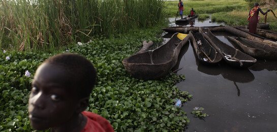 Kind steht im Vordergrund, Boote sind im Hintergrund zu sehen in Südsudan.