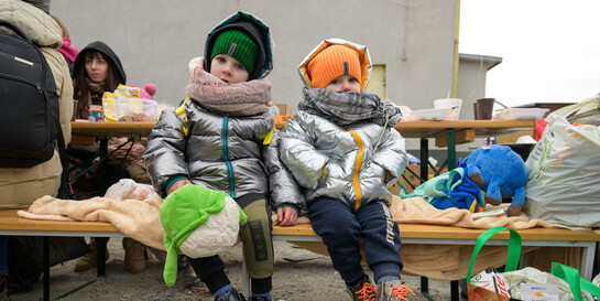 Zwei aus der Ukraine geflüchtete Kinder sitzen auf einer Bank.