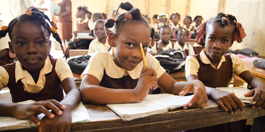Drei Schülerinnen sitzen an ihren Aufgaben in einer Schule in Haiti