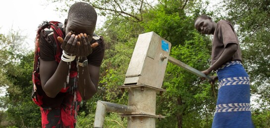 Im Südsudan trinken zwei Menschen Wasser aus einem Brunnen.