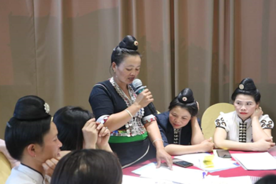 Eine vietnamesische Frau hält ein Mikro in der Hand und spricht vor anderen Frauen