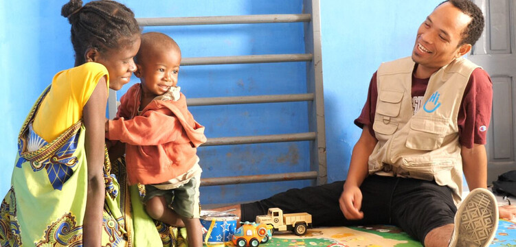 Ein Mitarbeiter von Handicap International bei einer Therapie mit Mutter und Kind 