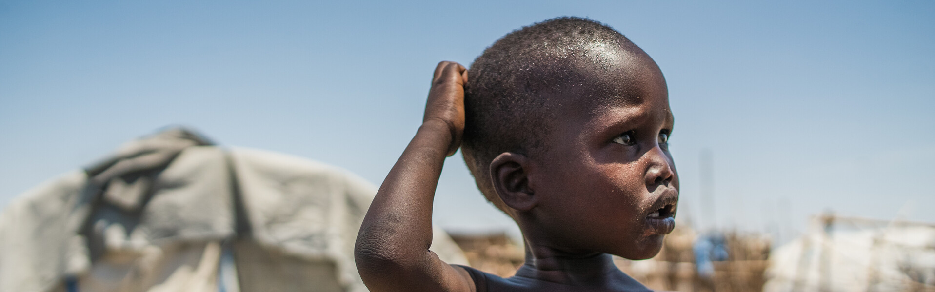 Ein Junge im Südsudan steht vor einem Flüchtlingszelt.