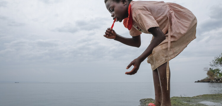 Ein Mädchen putzt sich die Zähne an einem See in Uganda