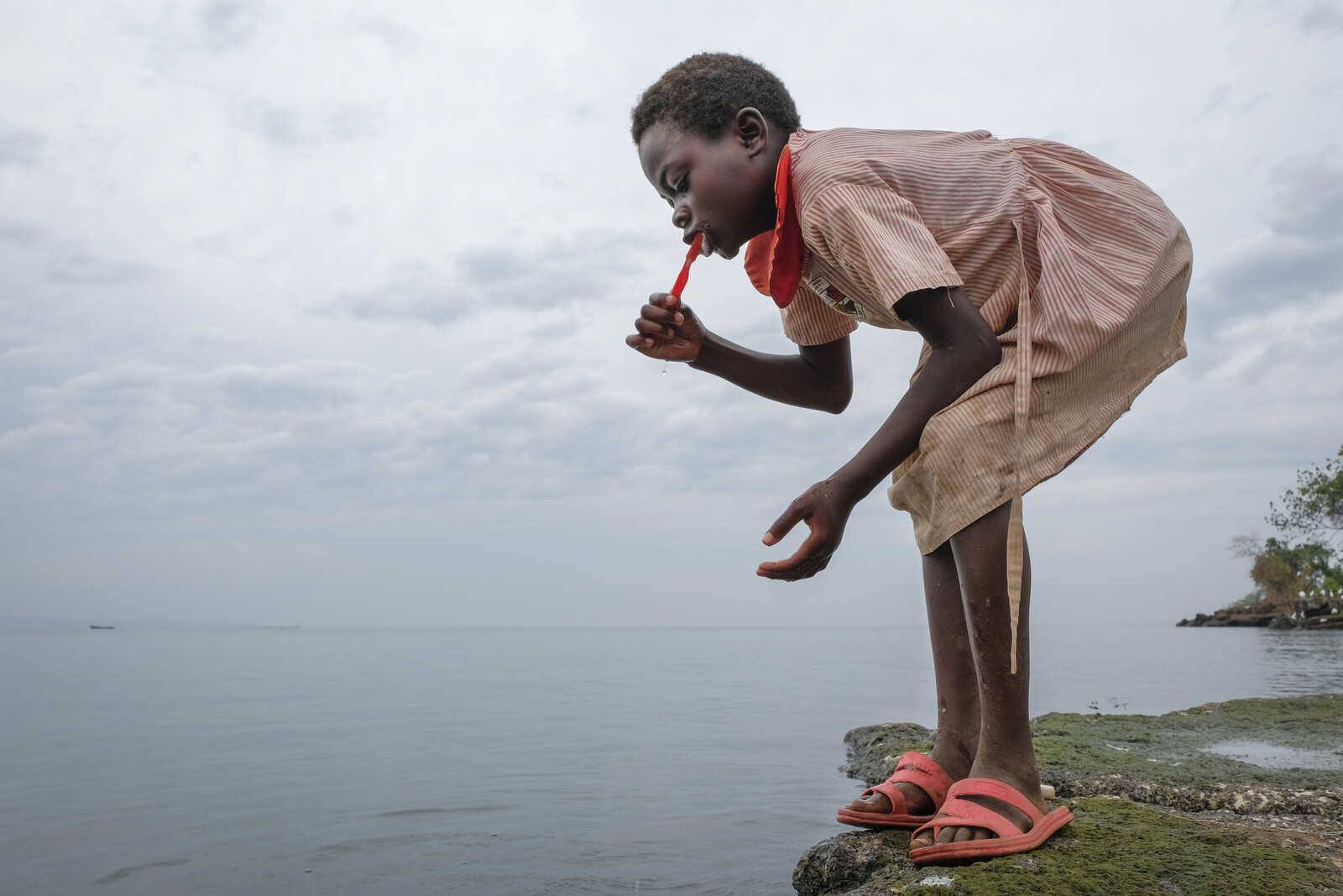 Ein Mädchen putzt sich die Zähne an einem See in Uganda