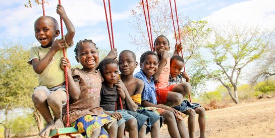 Kinder sitzen auf einer Schaukel in Afrika und freuen sich.