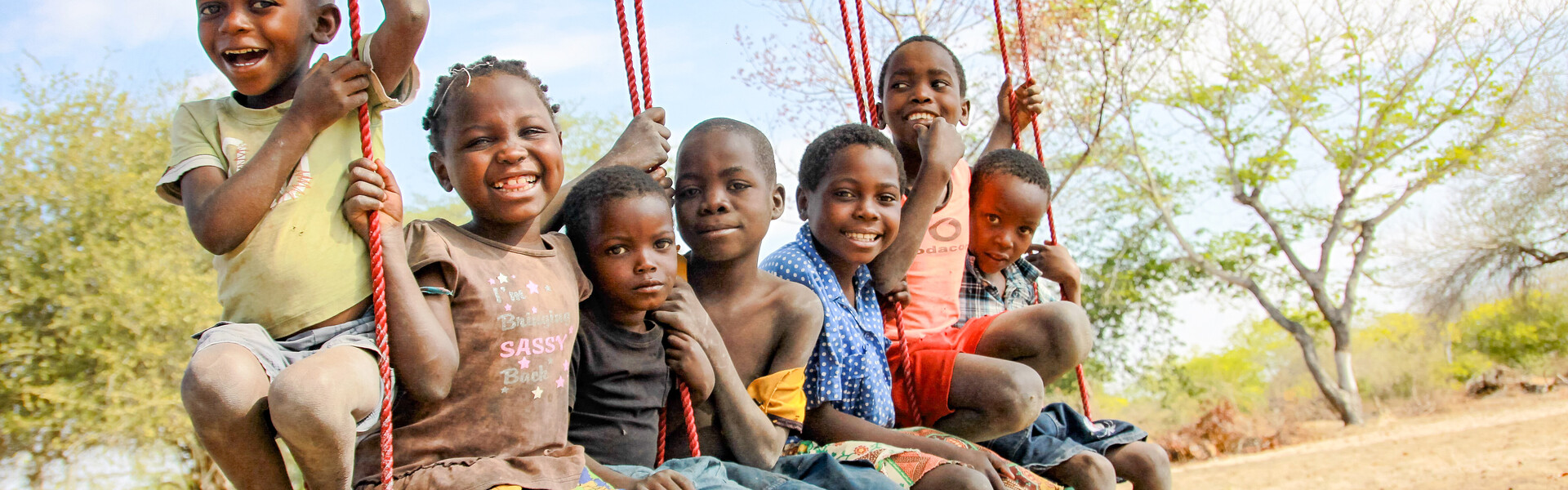 Kinder sitzen auf einer Schaukel in Afrika und freuen sich. © CARE/ Johanna Mitscherlich